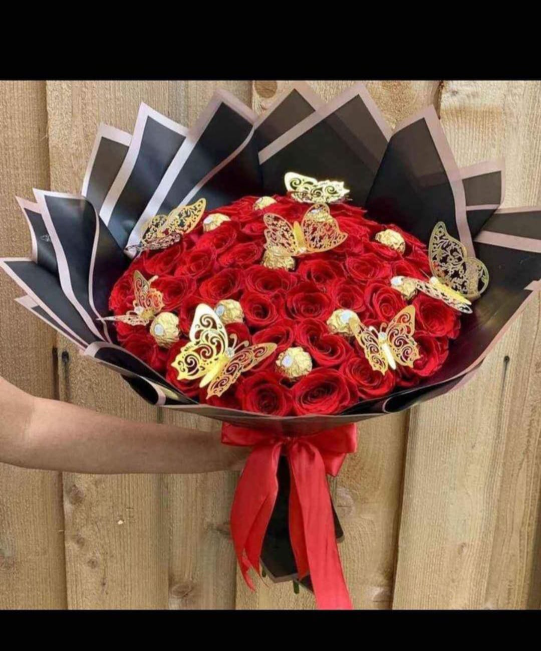 Ramo de rosas rojas con mariposas doradas y bombones, envuelto en papel negro con lazo rojo